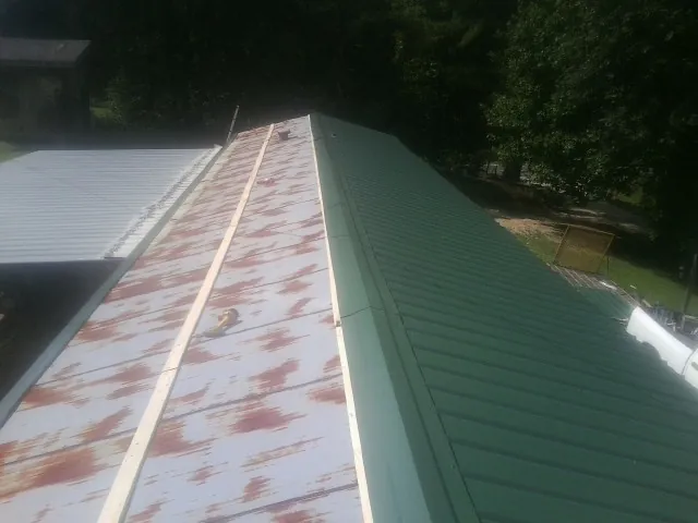 Old rusted panels beside newly installed green metal roofing — Wind Damage Roof Repair by Roofing Brothers in Fork