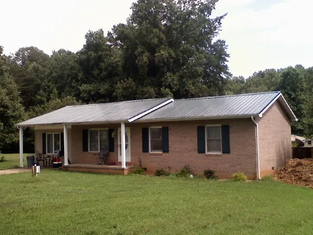 Gray metal roof on a brick ranch house with a side carport in Fork