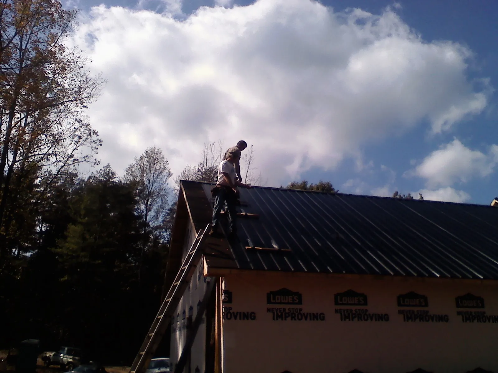 Roofer fastening dark metal panels high against a cloudy sky, from a Roof Inspection job in Fork